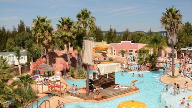 A resort pool area with multiple water features, palm trees, and a wooden deck. - Beachside Family Holiday Home (Hyères)