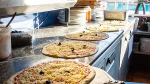 A kitchen counter with multiple pizza doughs topped with cheese and olives, a pizza box, and kitchen utensils. - Beachside Family Holiday Home (Hyères)