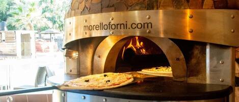 Horno para pizza al aire libre con baldosas de piedra, una pantalla digital, una pizza en su interior y un nombre de sitio web a la vista.