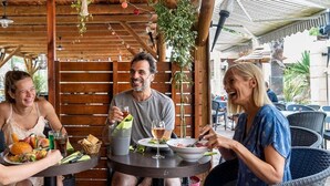 A wooden outdoor dining area with tables, chairs, hanging plants, and a covered roof. - Beachside Family Holiday Home (Hyères)