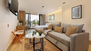 Una habitación de hotel moderna con sofá, una mesita, televisor montado en la pared y balcón con vistas.