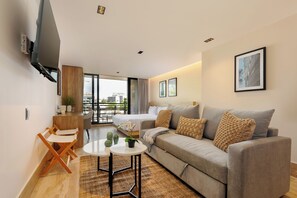 Ein modernes Hotelzimmer mit einer Couch, einem kleinen Tisch, einem an der Wand befestigten Fernseher und einem Balkon mit Blick.