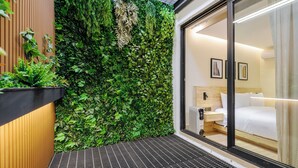 Una habitación de hotel moderna con un ventanal grande, una cama, una mesita de noche y una pared con jardín vertical.