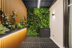 Un pasillo estrecho con una pared verde cubierta de plantas, un revestimiento de listones de madera en un lado y un piso de rejilla negra.
