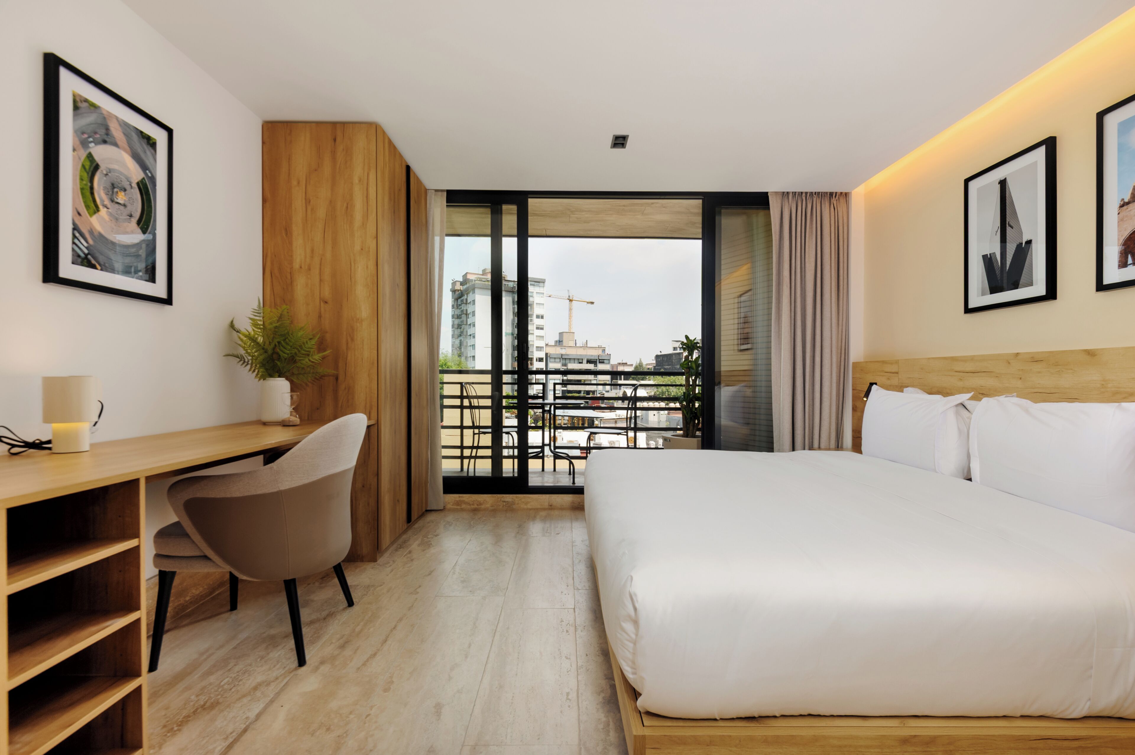 Ein Hotelzimmer mit Bett, Schreibtisch, Stuhl und Blick auf die Stadt durch große Fenster.