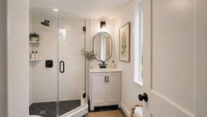 A bathroom with a glass-enclosed shower, a white vanity with a mirror, and a framed artwork on the wall. - Baiting Hollow Waterfront, Private Beach & Stunning Sunsets (Riverhead)