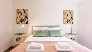 Een keurig ingerichte hotelkamer met een bed, twee nachtkastjes met lampen, een hoofdeinde en twee bloemschilderijen aan de muur.