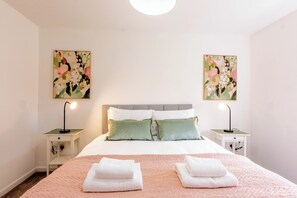 Ein ordentlich eingerichtetes Hotelzimmer mit einem Bett, zwei Nachttischen mit Lampen, einem Kopfteil und zwei floralen Bildern an den Wänden.