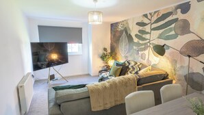 Een moderne woonkamer met een bank, een televisie, een eettafel en een groot abstract schilderij aan de muur.