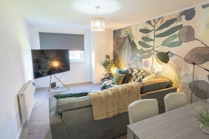 Ein modernes Wohnzimmer mit einer Couch, einem Fernseher, einem Esstisch und einem großen, abstrakten Wandbild.