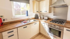 Een keuken met houten kastjes, een rvs fornuis, een spoelbak en een raam met uitzicht op een huis.