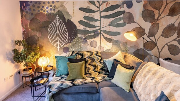 Een gezellige woonkamer met een bank, een bijzettafeltje, een lamp en een muurschildering.