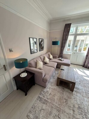 A living room with a sofa, a coffee table, a lamp, and a radiator. - Guildford Apartment with Free Parking & Garden (Guildford)