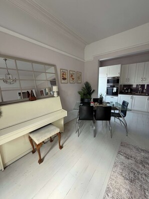 A modern kitchen with white cabinets, a dining area with a glass table and chairs, and a piano in the corner. - Guildford Apartment with Free Parking & Garden (Guildford)