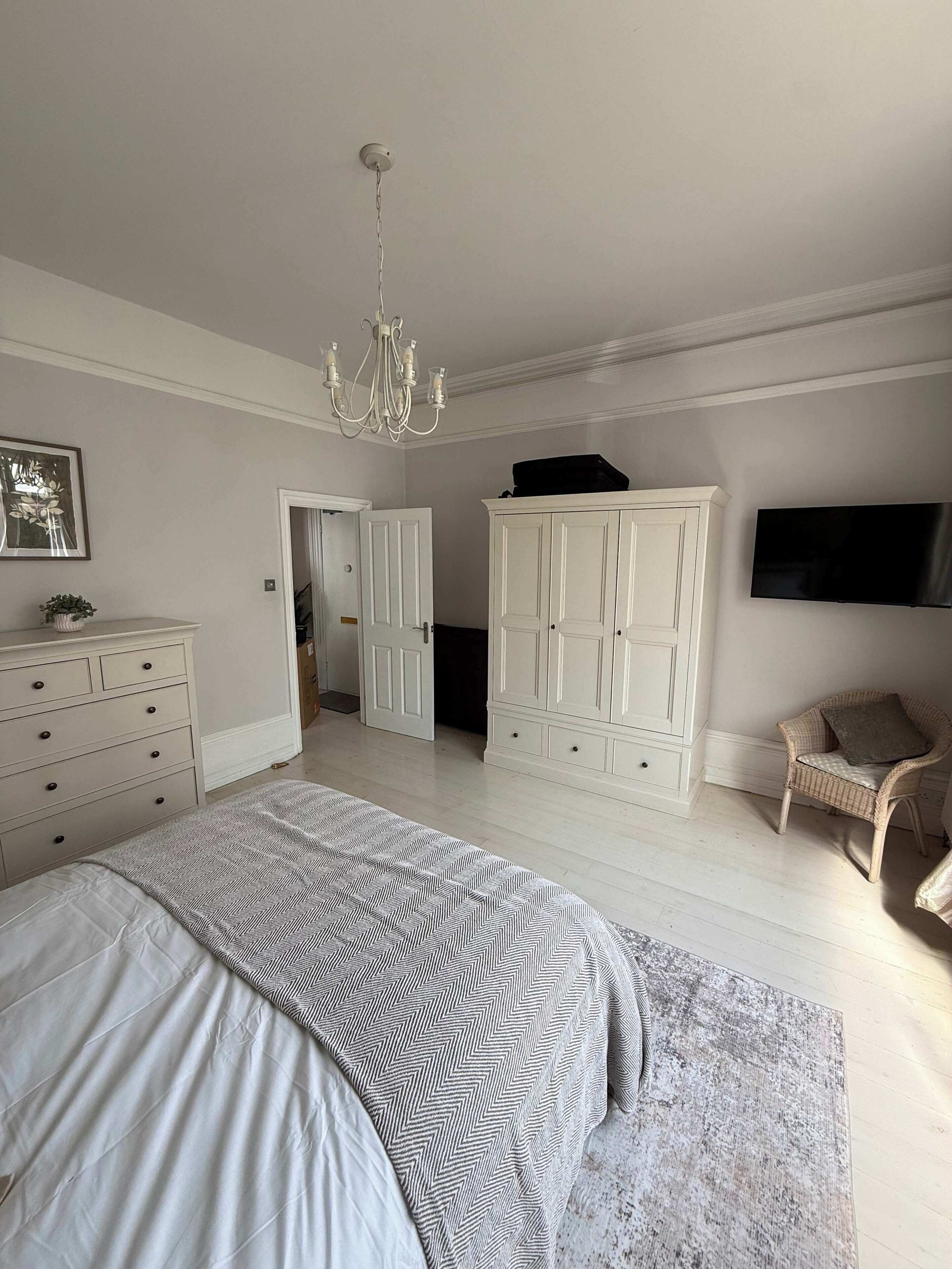 A bedroom with a bed, dresser, wardrobe, chair, and a TV.