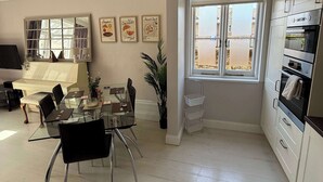 A modern kitchen with a dining area, featuring a glass table, black chairs, and a window with blinds. - Guildford Apartment with Free Parking & Garden (Guildford)