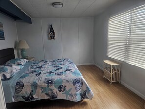 A bedroom with a bed, a nightstand, a lamp, a small table, a window with blinds, and a wall-mounted decoration. - Perfect 2-bedroom house with community pool near beaches in Fort Myers (Fort Myers)
