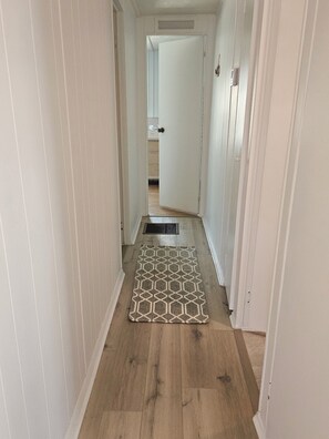 A narrow hallway with wooden flooring, a patterned rug, and a door leading to another room. - Perfect 2-bedroom house with community pool near beaches in Fort Myers (Fort Myers)