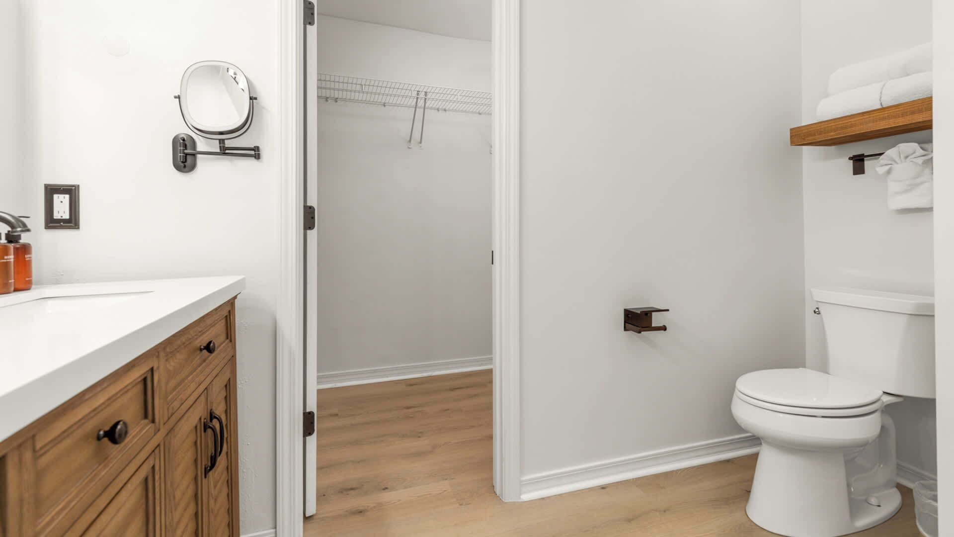 A bathroom with a white toilet, a wooden vanity, a mirror, and a towel rack.