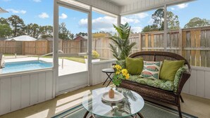 A screened porch with a wicker sofa, a glass table, and a view of a backyard pool. - Sunny Daze - 3bdr With Pool (Orange Beach)