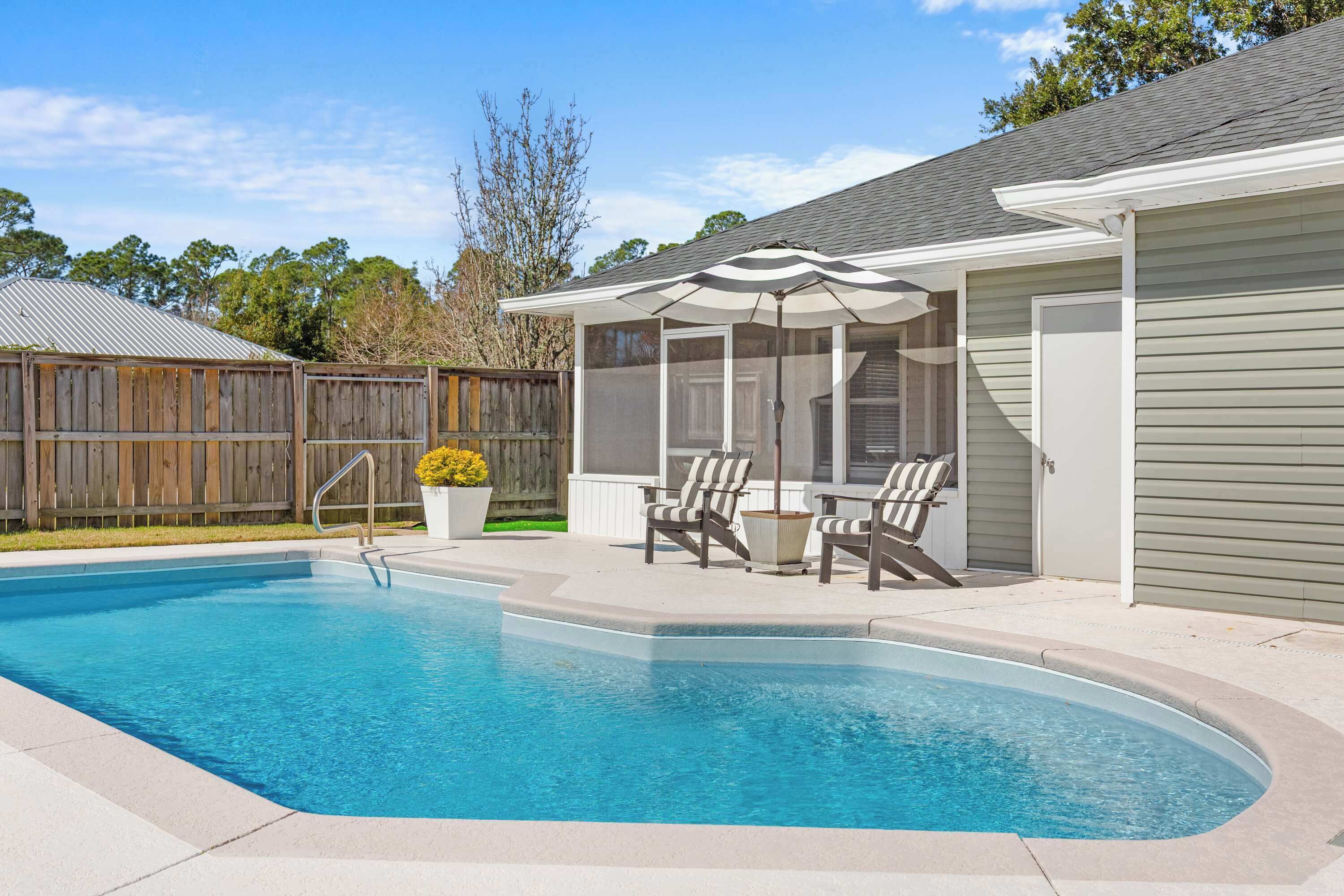 A swimming pool with a covered patio area, a wooden fence, and a house with a garage.