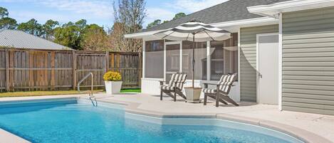 Une piscine avec un patio couvert, une clôture en bois et une maison avec un garage.