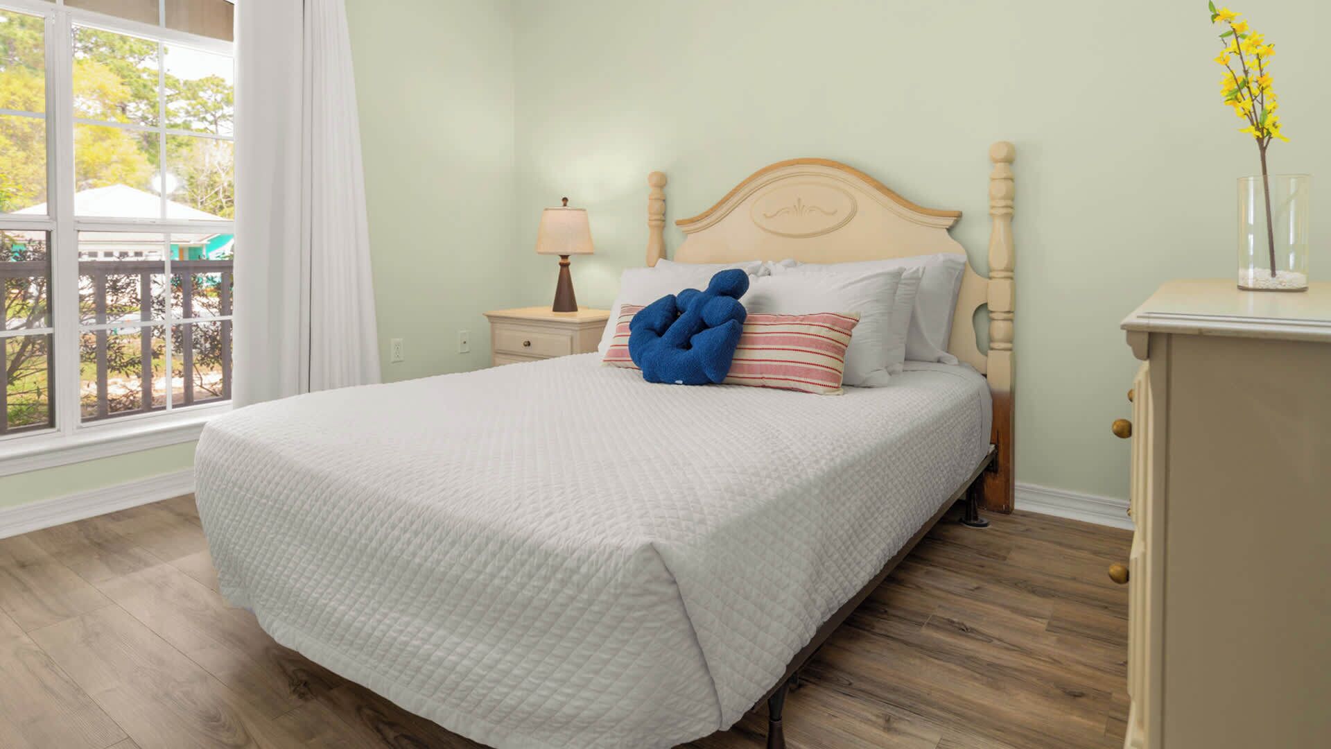 Ein ordentlich gemachtes Bett mit weißer, gesteppter Bettdecke, einem Holz-Kopfteil und einem blauen Zierkissen.