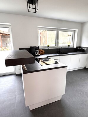 A modern kitchen with a central island, a built-in oven, and a window providing natural light. - The Cube - Modern architect's house in the town center (Stegaurach)