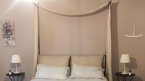 Una cama con dosel y cuatro columnas, con un edredón blanco texturizado, dos mesitas de noche con lámparas y un adorno de barco en la pared.