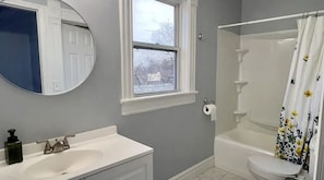 A bathroom with a sink, mirror, window, toilet, and shower.