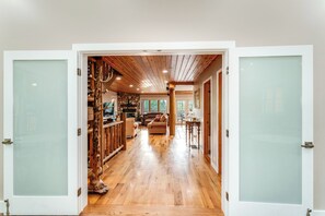 A spacious hallway with wooden flooring, a stone fireplace, and a view of the outdoors. - The Chalet at North Star Ranch - Secluded 40 Acres (Whitefish)