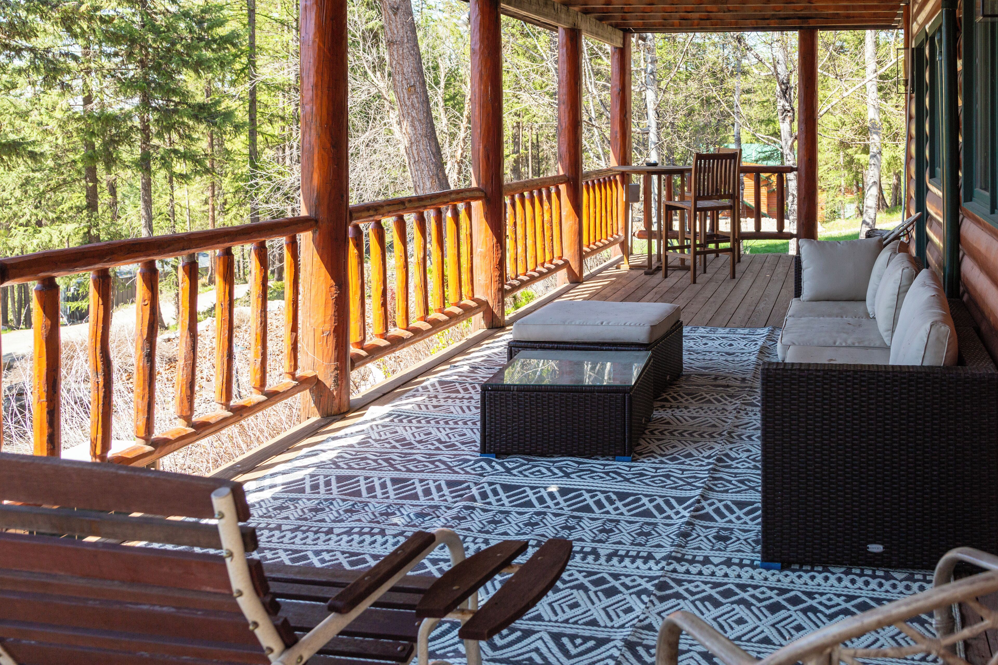 A covered outdoor area with a wooden deck, seating arrangements, and a view of the surrounding forest.