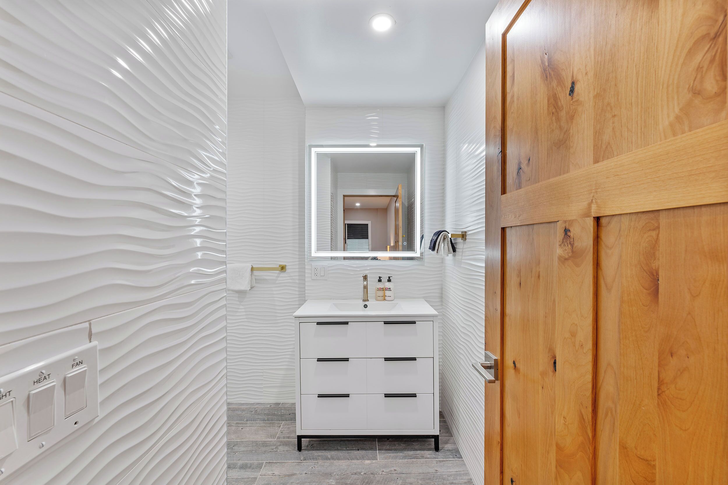 Un baño con tocador blanco, espejo y puerta de madera.
