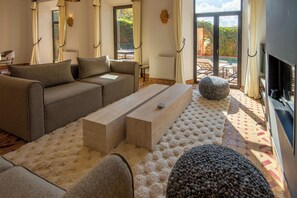 A modern living room with a sofa, coffee table, and ottoman, a fireplace, and a view of the outdoors. - Golf villa amelkis 4 bedrooms (Marrakech)