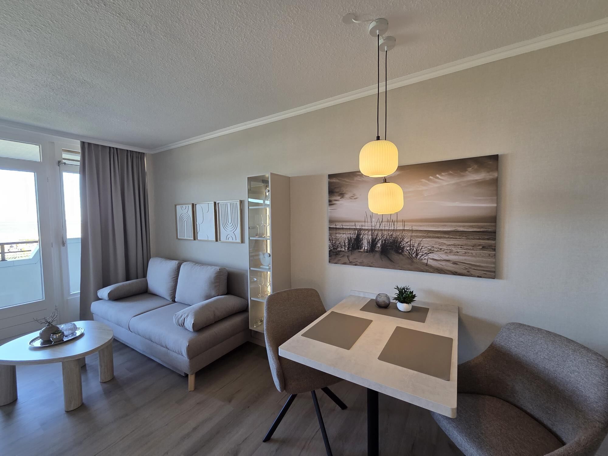 Un salon moderne avec un canapé, une table à manger et un tableau représentant une scène de plage.