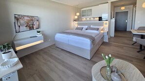 Ett modernt sovrum med en stor säng, sängbord, en tv och en matplats med ett bord och stolar.