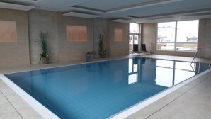 En inomhuspool med klart vatten, kaklade väggar och krukväxter.