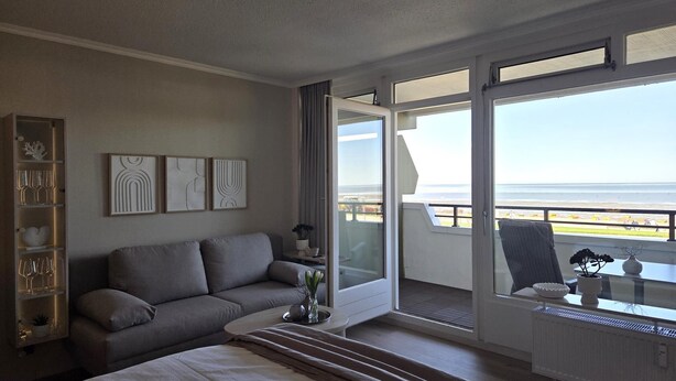 Ett hotellrum med en säng, en soffa, ett matbord, utsikt över stranden och en balkong.