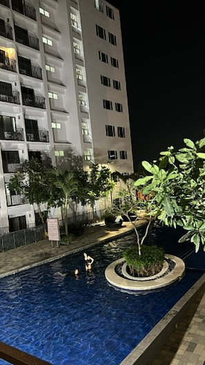 Ein Nachtblick auf einen Hotelpoolbereich mit einem Gebäude im Hintergrund.