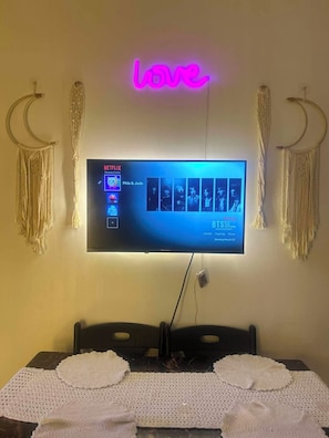 Ein Flachbildfernseher an der Wand, darüber ein Neonzeichen.