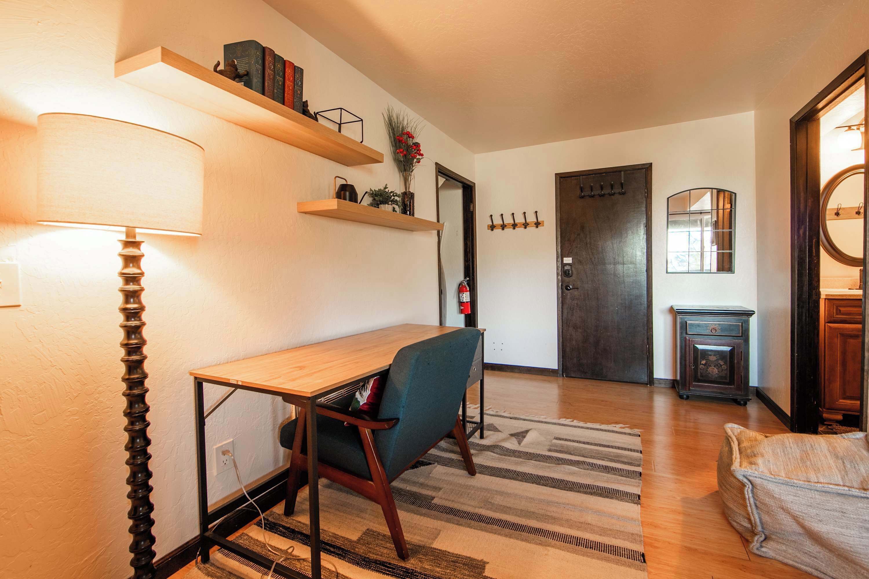 A room with a desk, chair, lamp, shelves, and a door.