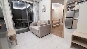 Ein modernes Wohnzimmer mit Sofa, einem kleinen Tisch, einer Küchenzeile mit Geräten und einer Glastür, die auf einen Balkon führt.