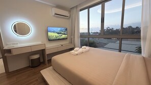 Ein modernes Hotelzimmer mit einem großen Bett, einem Fernseher, einem Nachttisch, einem Spiegel und Blick auf die Stadt.