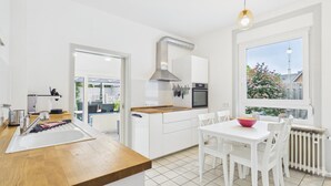 A modern kitchen with white cabinets, a wooden countertop, and a dining area with white chairs.