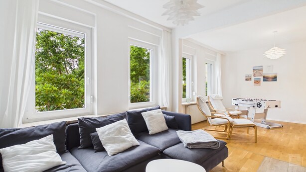 A modern living room with a grey sofa, white cushions, and a foosball table.