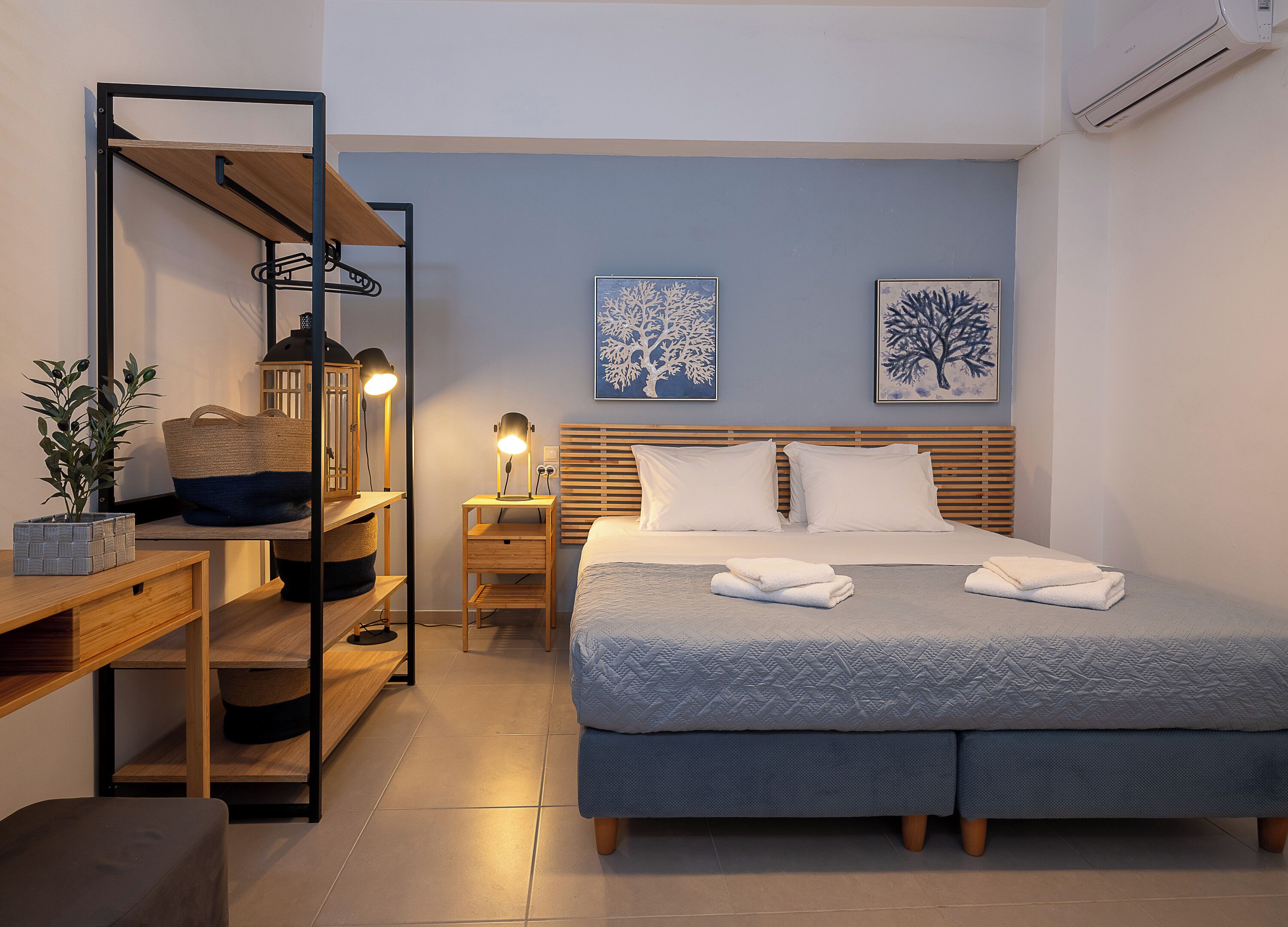 A neatly arranged bedroom with a bed, bedside tables, a desk, and a shelf unit.