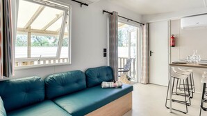 A modern room with a teal sofa, a dining area with bar stools, and a kitchen with an air conditioning unit. - Adriatic Family Retreat With Terrace (Brtonigla)