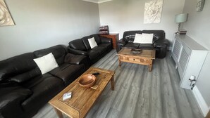 Una sala de estar con un sofá de cuero negro, una mesa de centro de madera y un sillón de cuero negro.