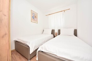 Un dormitorio con dos camas, ropa de cama blanca, una puerta de madera y un cartel en la pared.