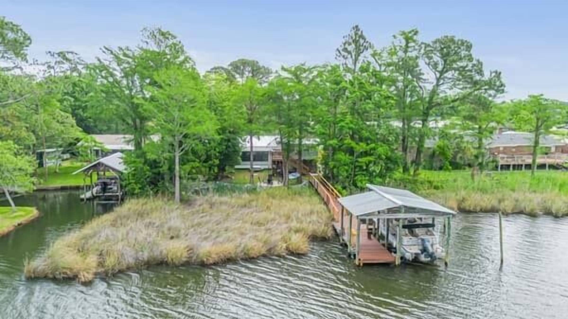 A houseboat with a covered deck and a small dock, surrounded by water and greenery.